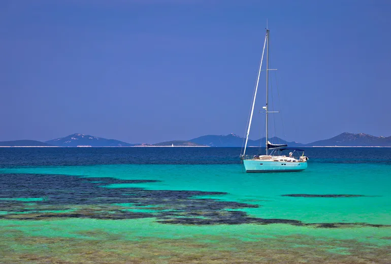 A single sailboat anchored in turquoise shallows with low Croatian islands behind