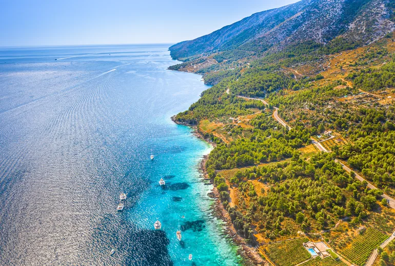 Aerial of a Croatian island coastline with vineyards and sailboats moored offshore
