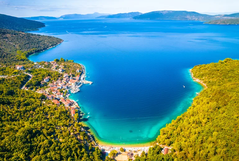 Aerial of a deep turquoise bay ending in a beach beside a small waterfront village
