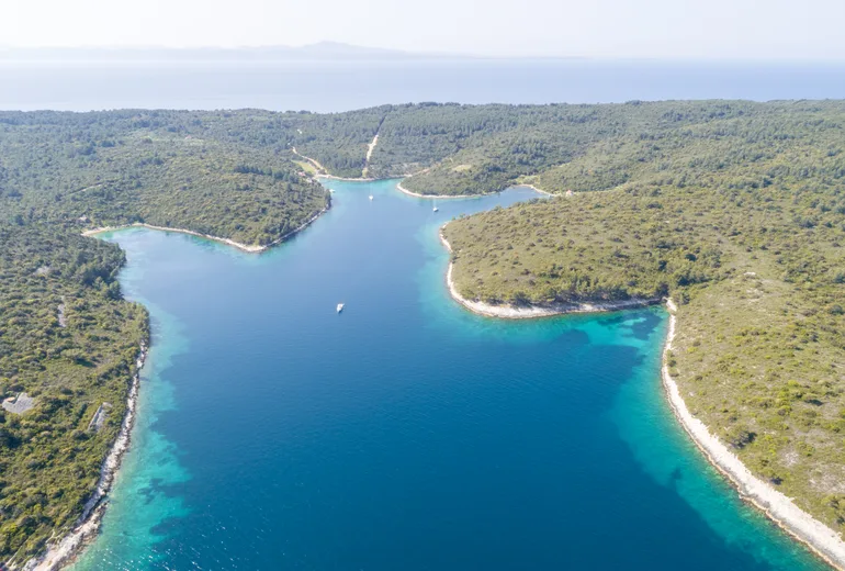 Aerial of a long sheltered island inlet with a few anchored sailboats in clear water