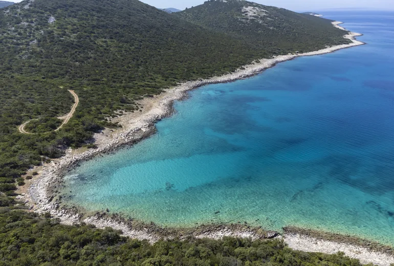 Aerial of a remote turquoise cove with a white pebble rim and low scrub hills