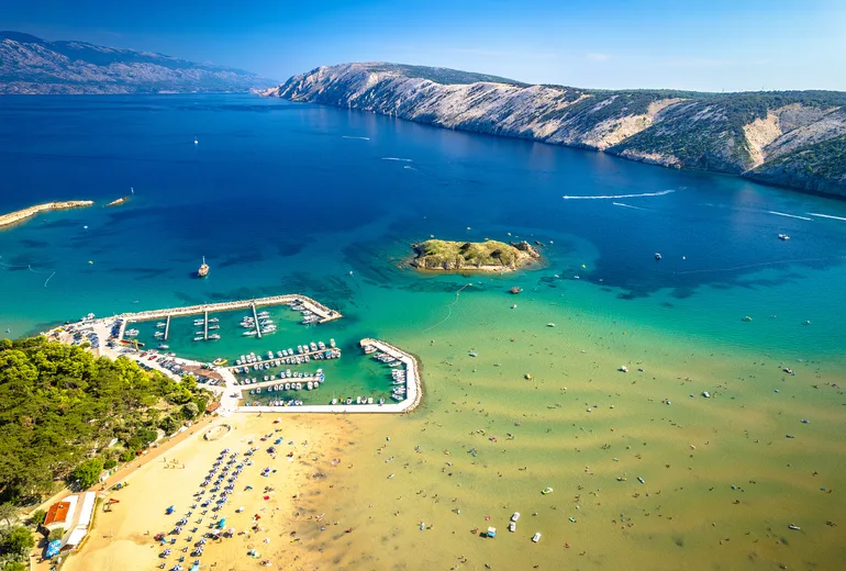 Aerial of a sandy beach, small marina and islet on Rab island