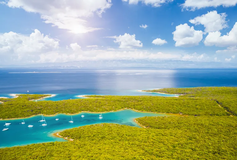 Aerial of forested Croatian island bays with anchored sailboats in bright low sun