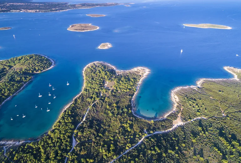 Aerial of green islets and coves dotted with anchored sailboats in Croatia