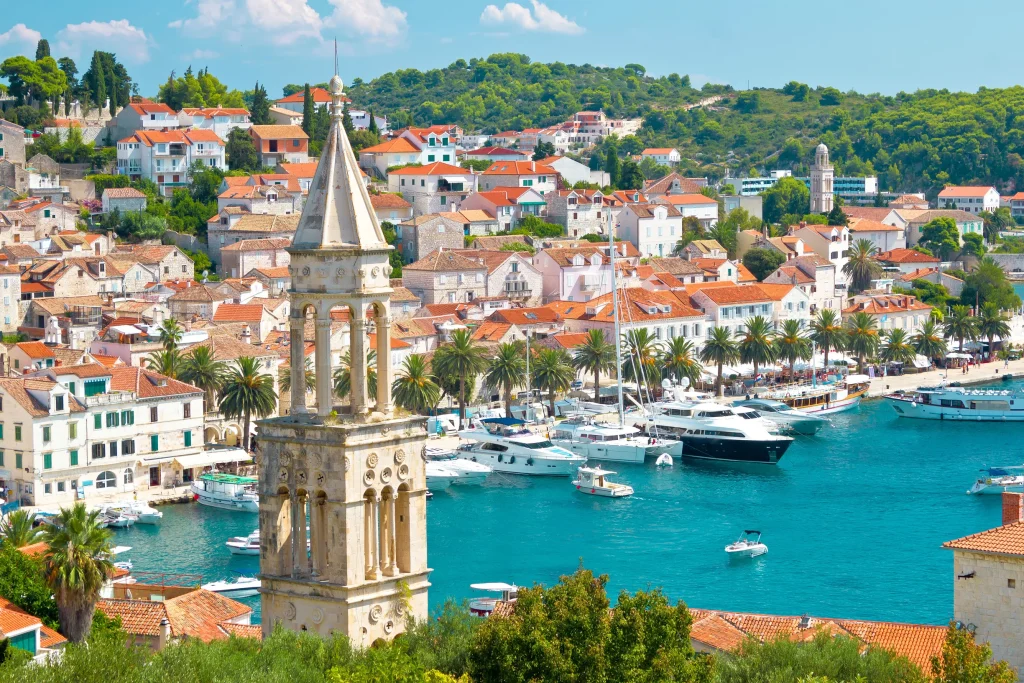 Hvar town bell tower, palm-lined waterfront and yacht-filled harbor viewed from above