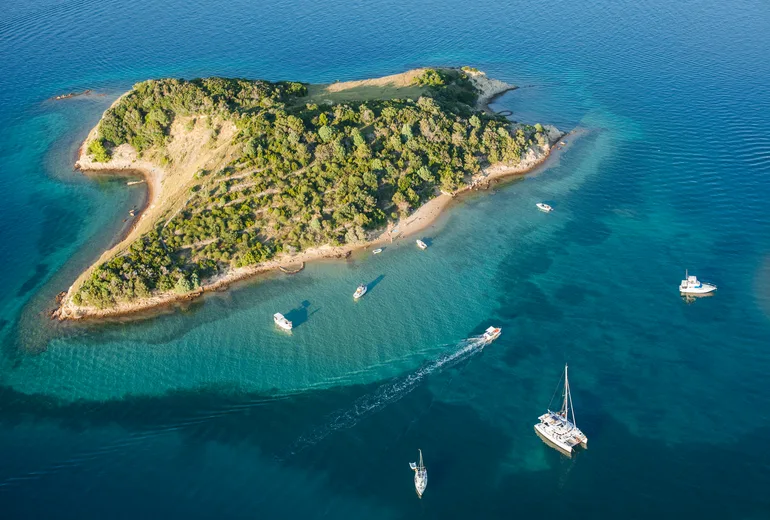 Catamaran and motorboats cruising past a small Croatian island