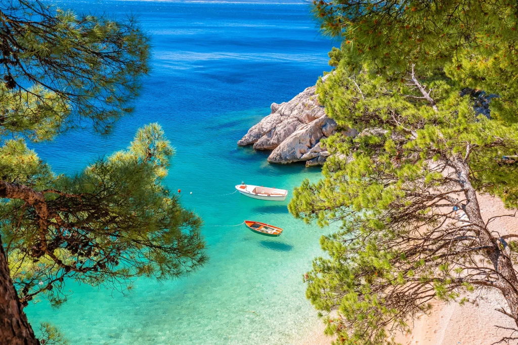Turquoise cove with pebble beach, two small boats framed by pine trees