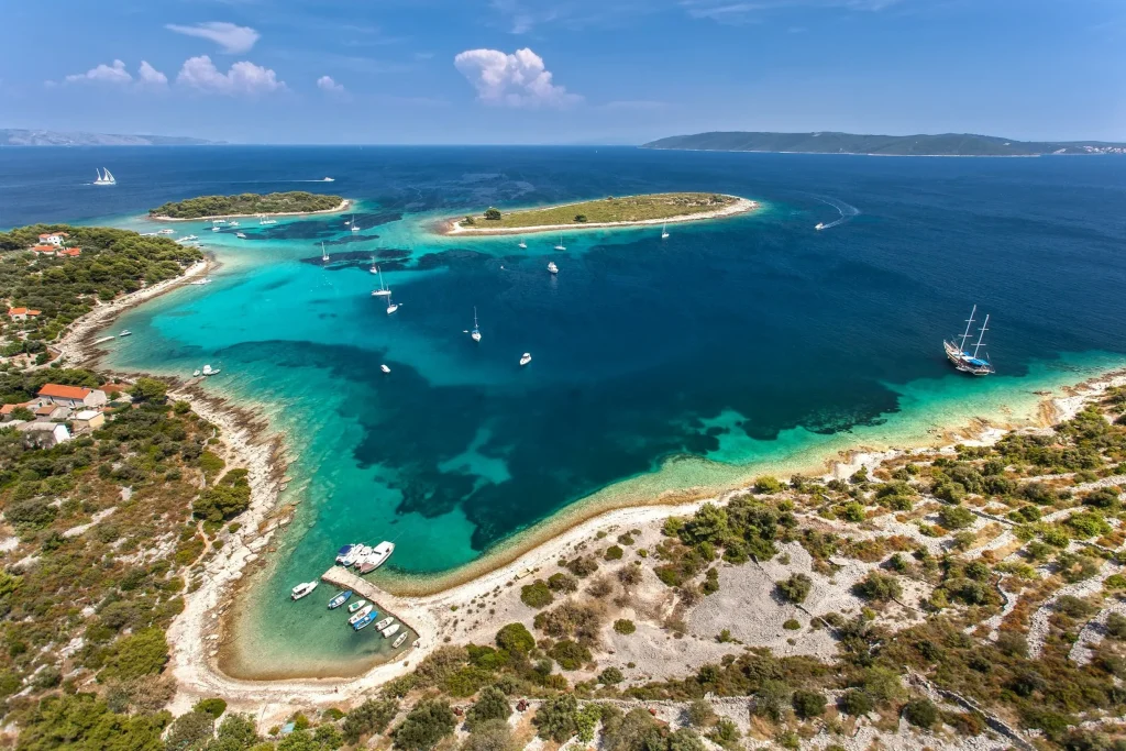 Aerial of turquoise Krknjasi Blue Lagoon, Drvenik Veli, with anchored sailboats and gulet