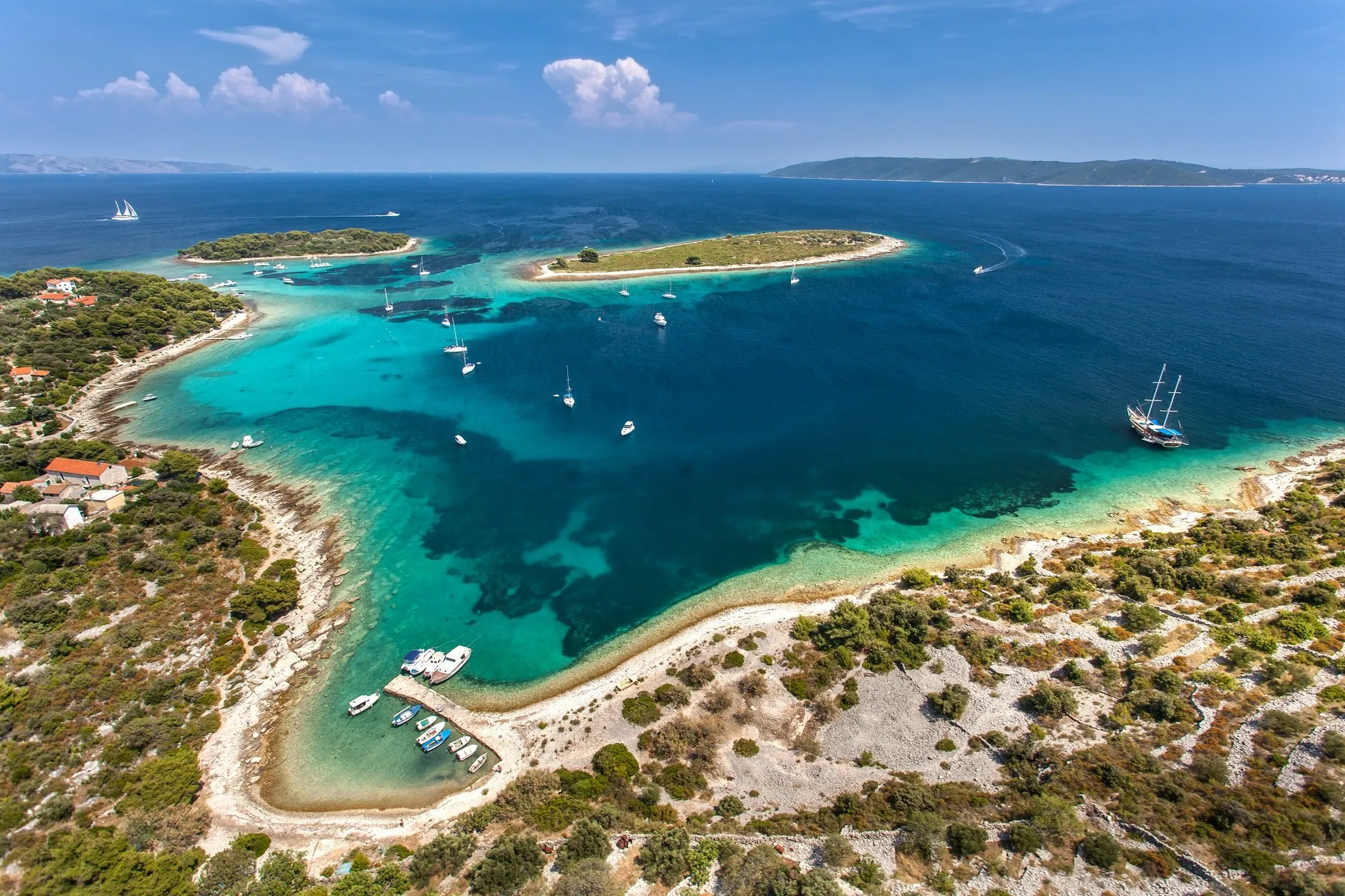 Aerial of turquoise Krknjasi Blue Lagoon, Drvenik Veli, with anchored sailboats and gulet
