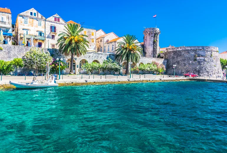 Korčula old town walls and towers rising above clear turquoise waterfront