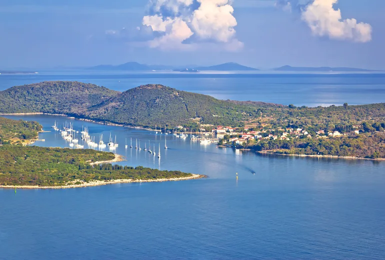 Row of sailboats moored in a sheltered channel beside a small Croatian island village