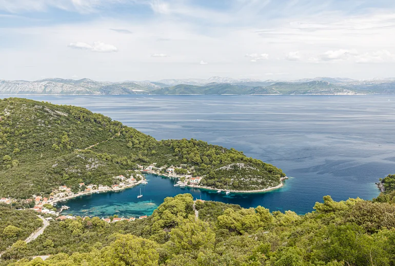 Sheltered island cove hamlet with an anchored sailboat and mainland mountains across the channel