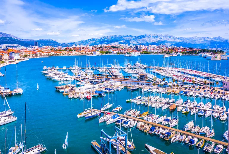 Split city marina packed with sailboats, with mountains rising behind