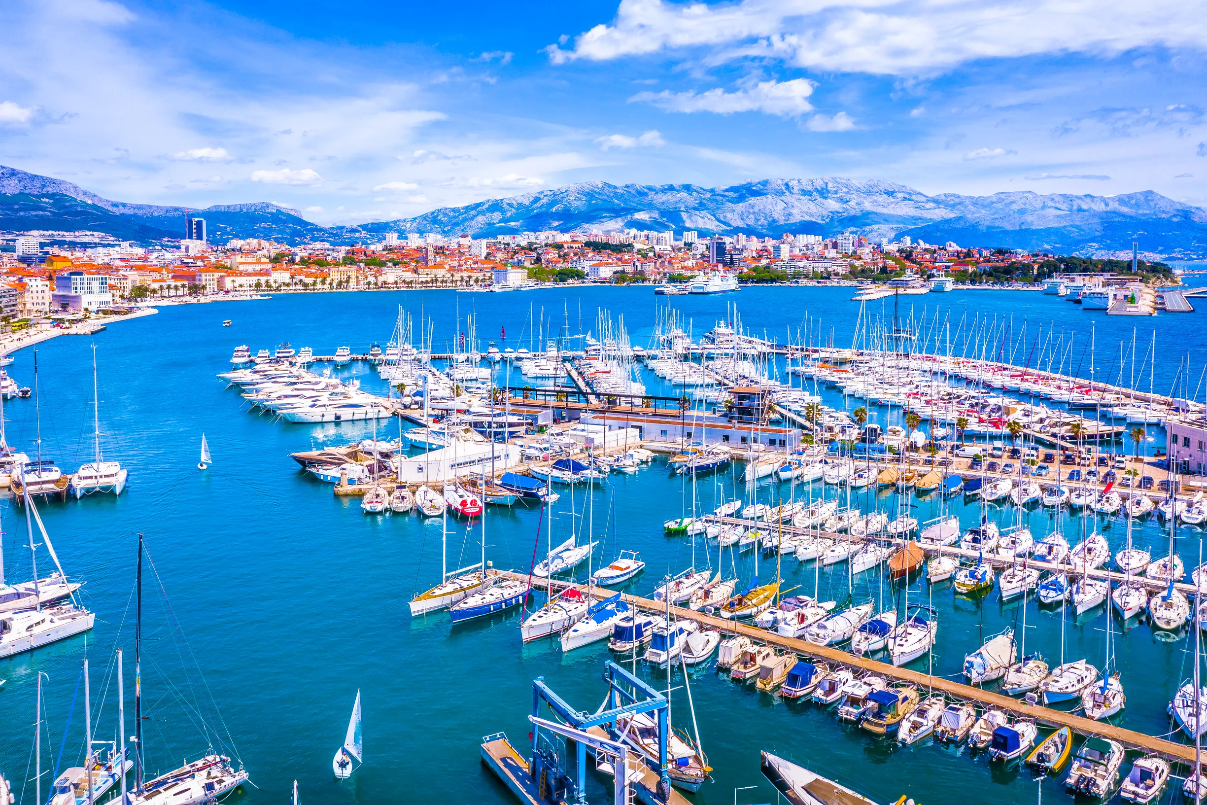 Split city marina packed with sailboats, mountains rising behind