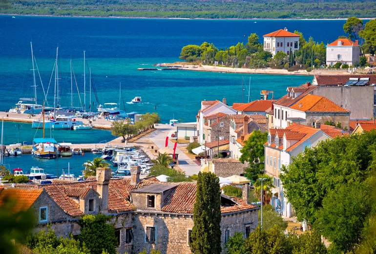 Stone village rooftops above a small harbor with moored boats and masts