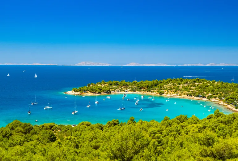 Turquoise bay anchorage with yachts, pine shores and distant Croatian islands