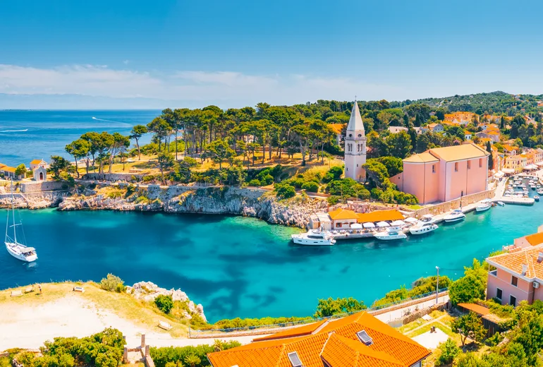 Veli Losinj cove with a pink church, bell tower and moored boats